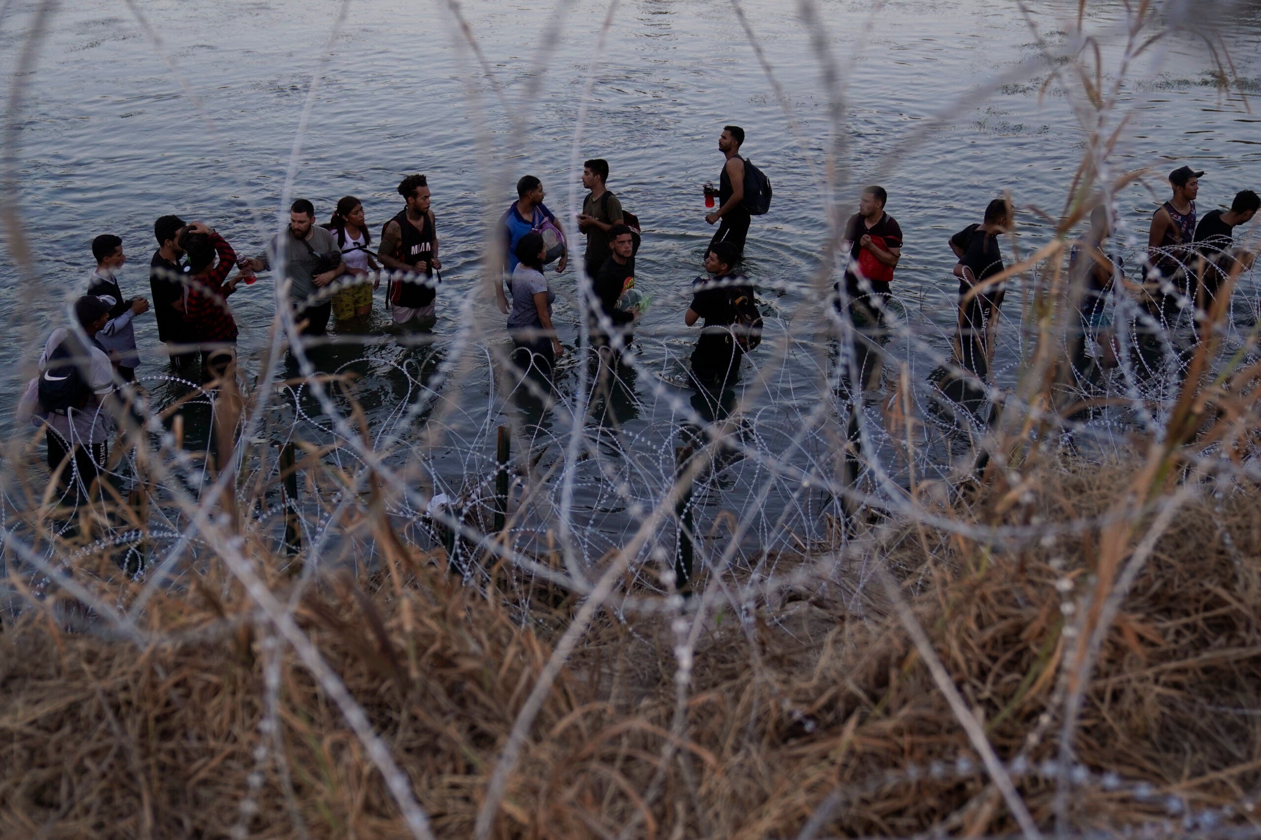 FILE - Migrants wait to climb over concertina wire after they crossed the Rio Grande and entered the U.S. from Mexico, Saturday, Sept. 23, 2023, in Eagle Pass, Texas.