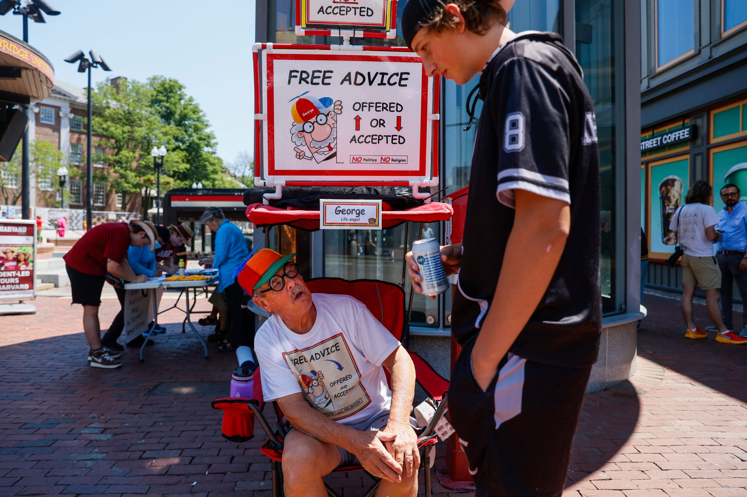George Vaill, self-defined Life-oligist, offers advice to 15-year-old Stefan Alexandrov while sitting in Harvard Square on June 1, 2023. Known to passersby as the "free advice" guy, Vaill doles out counsel to strangers in Harvard Square from a folding chair.